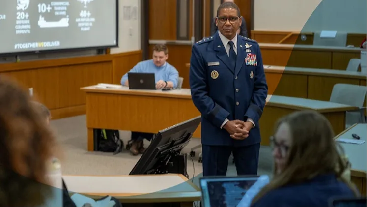 A senior military officer in dress uniform addressing people seated in a briefing room