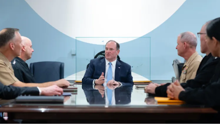 A civilian official in a suit meeting with uniformed officers around a conference table