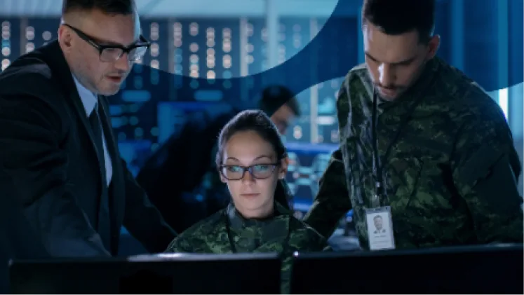 Two uniformed personnel and a civilian analyst reviewing monitors in a darkened operations centre