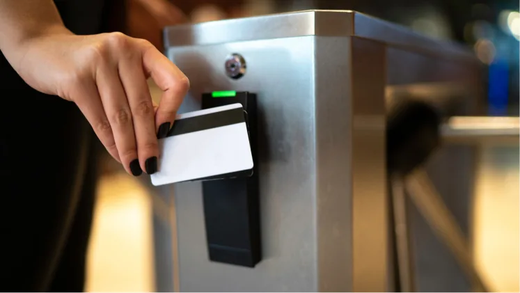 A hand holding an access card up to the reader on a security turnstile