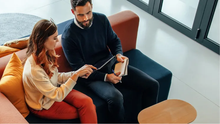 Two colleagues reviewing notes together on an office sofa