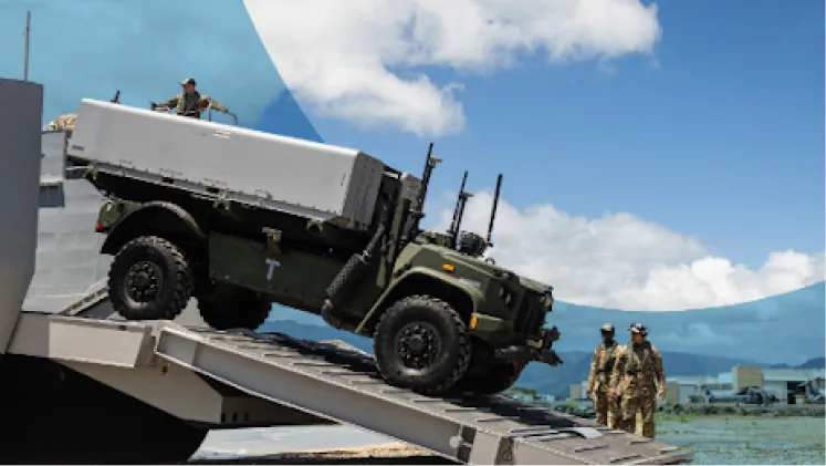 A military transport vehicle driving down a landing craft ramp as personnel look on