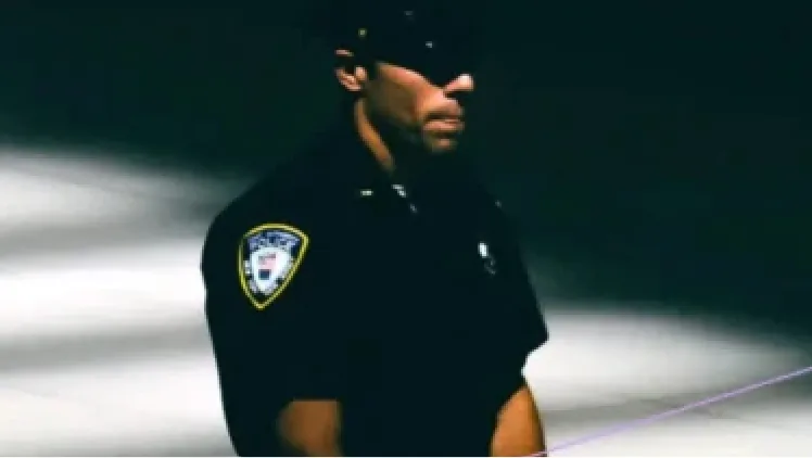 A police officer in uniform, seen from the side in low light